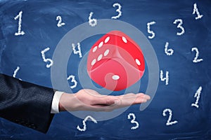 Businessman hand and big red dice with random numbers on blue background