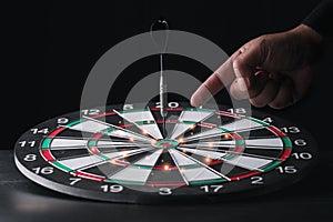 Businessman hand in black suite pointing black dart on center of target board on vintage table meaning of investment and achieveme