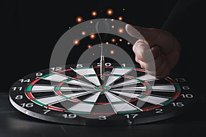 Businessman hand in black suite showing thumb up on center of target board with black dart on vintage table meaning of investment