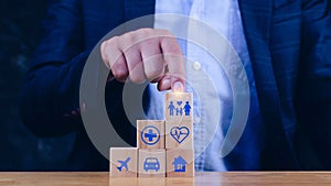 Businessman hand choose wooden blocks with icons of various types of insurance, protection icons for safety family insurance. Life