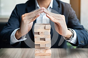 Businessman hand cover wooden block on the tower