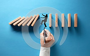 Businessman hand drawing silhouette of a man in panic against collapsing wooden dominos on blue background. Business crisis and