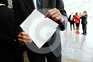Businessman hand draws an invitation from a white envelope. Blank template to fill with text, people defocused on background