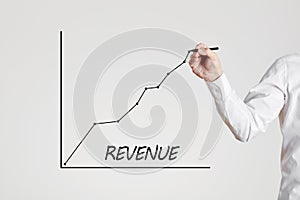 Businessman hand draws a rising line graph with the word revenue. Increase in business revenue