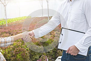 Businessman hand hold contract and asian woman farmer success deal contract in greenhouse hydroponic organic farm ,Small business