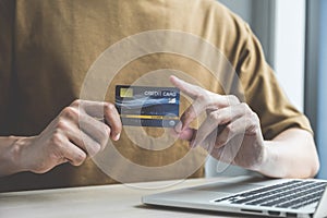 Businessman hand hold credit card to online shopping on laptop computer from home, payment e-commerce, internet banking, spending