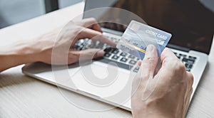 Businessman hand hold credit card to online shopping on laptop computer from home, payment e-commerce, internet banking, spending