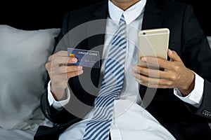 Businessman hand hold mock-up credit card for online shopping on smartphone from hotel bedroom, payment e-commerce, internet