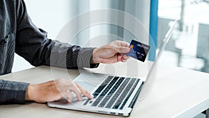 Businessman hand holding credit card to online shopping from home with laptop, payment e-commerce, internet banking, spending