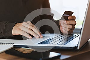 Businessman hand holding credit card with using laptop for online shopping while making orders at home. business