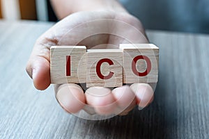 Businessman hand holding ICO Initial Coin Offering word with wooden cube block, is the cryptocurrency industry equivalent to an