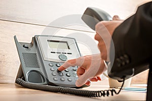 Businessman hand holding a landline telephone receiver dialing a photo