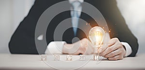 Businessman hand holding light bulb with icon on wood cube and   working on desk, Creativity and innovation are keys to success.Co