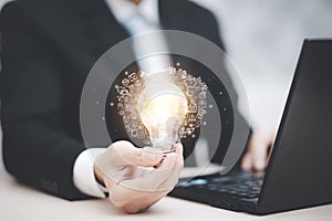 Businessman hand holding light bulb with icons and working on the desk, Creativity and innovation are keys to success.Concept of n