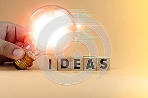 Businessman hand holding a light bulb and wood block with word Ideas. Innovation and creative concept