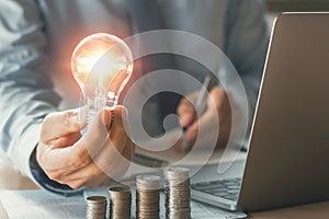 businessman hand holding lightbulb with stack money. concept saving energy and finance