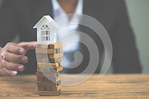 Businessman hand holding model white house on wood block. Investment risk and uncertainty in the real estate housing market