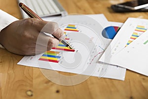 Businessman hand holding pen with graph and chart analysis paper