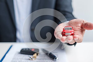Businessman hand holding red car toy with vehicle keyless, pen and contract document. buy and sale, insurance, rental and contract