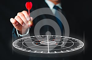 Businessman hand holding red dart put to centre of red target board.