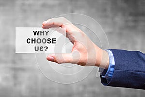 Businessman hand holding Why Choose Us? sign isolated on grey ba