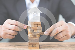 Businessman hand holding wood block with model white house. Investment risk and uncertainty in the real estate housing market