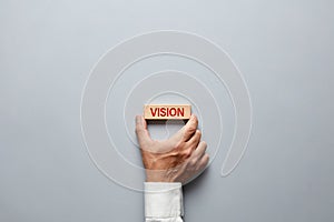 Businessman hand holding a wooden block with the word vision on gray background. Business vision statement