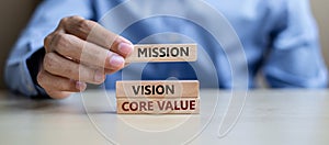 Businessman hand holding wooden building blocks with MISSION, VISION, CORE VALUE Concepts