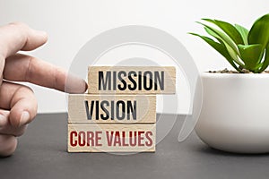 Businessman hand holding wooden building blocks with MISSION, VISION, CORE VALUE Concepts