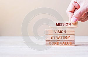 Businessman hand holding wooden building blocks with MISSION, VISION, CORE VALUE and STRATEGY word. Business concepts