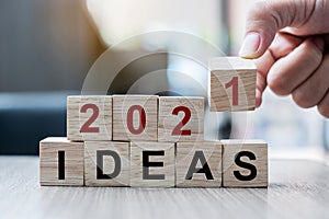 Businessman hand holding wooden cube with block 2021 IDEAS word on table background. Resolution, strategy, solution, goal,