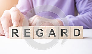 Businessman hand holding wooden cube block with REGARD business word on table background