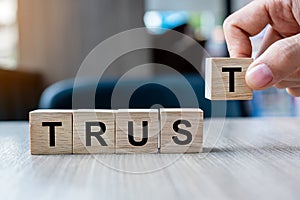 Businessman hand holding wooden cube block with TRUST business word on table background. Trustworthy, Truth, beliefs and agreement photo