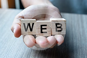 Businessman hand holding wooden cube block with WEB business word on table background. website, network, Database, and marketing