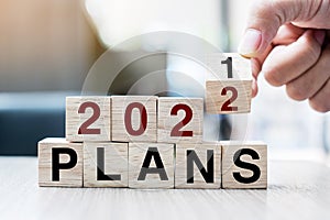 Businessman hand holding wooden cube with flip over block 2021 to 2022  Plans word on table background. Resolution, strategy,