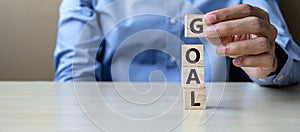 Businessman hand holding wooden cube with GOAL text on table background. success, strategy, solution and business concepts