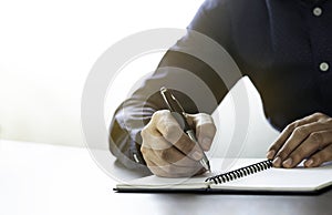 Businessman hand holding writing pen memo into notebook paper on table desk office.