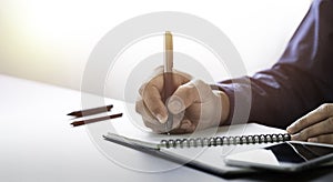 Businessman hand holding writing pen memo into notebook paper on table desk office.