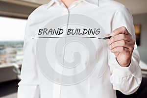 Businessman hand holds a pen and underlines the words brand building on virtual screen