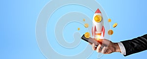 Businessman hand with phone and rocket with bitcoin on copy space background