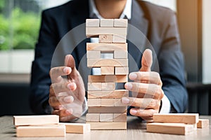 Businessman hand placing or pulling wooden block on the tower