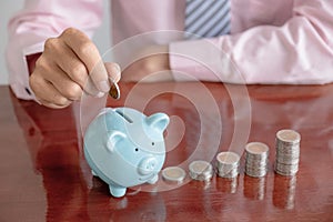 Businessman hand putting coin into blue piggy bank