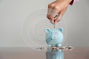 Businessman hand putting coin into blue piggy bank