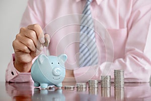 Businessman hand putting coin into blue piggy bank