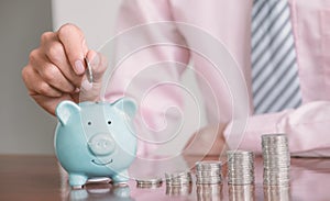 Businessman hand putting coin into blue piggy bank