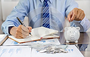 Businessman hand putting coin into blue piggy bank, saving money for future investment plan and retirement fund concept