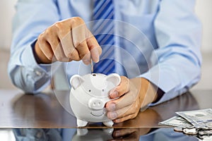 Businessman hand putting coin into blue piggy bank, saving money for future investment plan and retirement fund concept