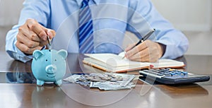 Businessman hand putting coin into blue piggy bank, saving money for future investment plan and retirement fund concept