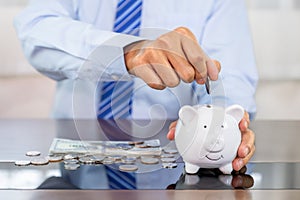 Businessman hand putting coin into blue piggy bank, saving money for future investment plan and retirement fund concept