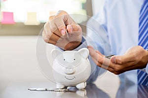 Businessman hand putting coin into blue piggy bank, saving money for future investment plan and retirement fund concept